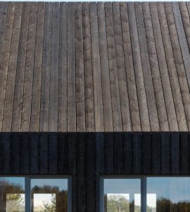 Façade d'une maison en planches de bois brûlées et des baies vitrées