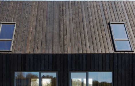 Façade d'une maison en planches de bois brûlées et des baies vitrées