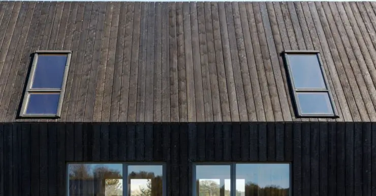 Façade d'une maison en planches de bois brûlées et des baies vitrées