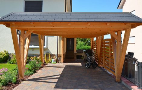 Un scooter garé sous un carport en bois devant une maison