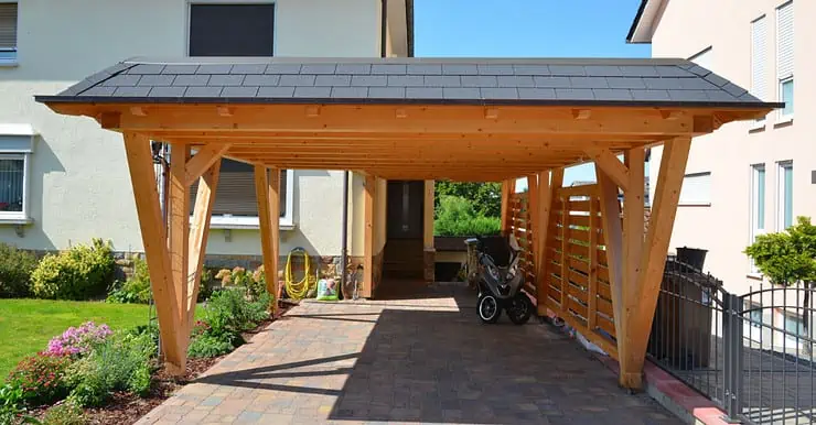 Un scooter garé sous un carport en bois devant une maison