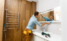 Un homme installant un miroir sur le mur d'une salle de bains