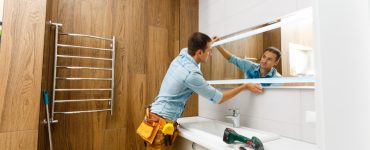 Un homme installant un miroir sur le mur d'une salle de bains