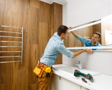 Un homme installant un miroir sur le mur d'une salle de bains