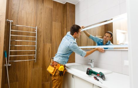 Un homme installant un miroir sur le mur d'une salle de bains