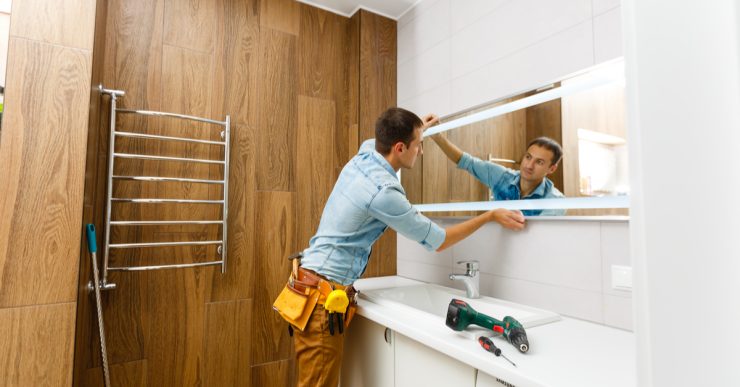 Un homme installant un miroir sur le mur d'une salle de bains