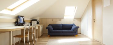 Une chambre aménagée dans le grenier avec un canapé bleu et un coin bureau