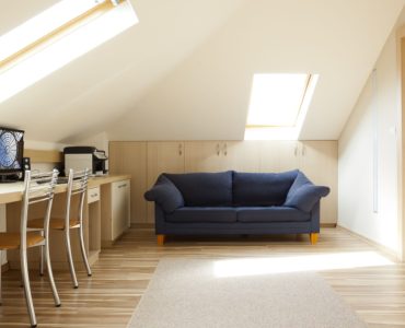 Une chambre aménagée dans le grenier avec un canapé bleu et un coin bureau