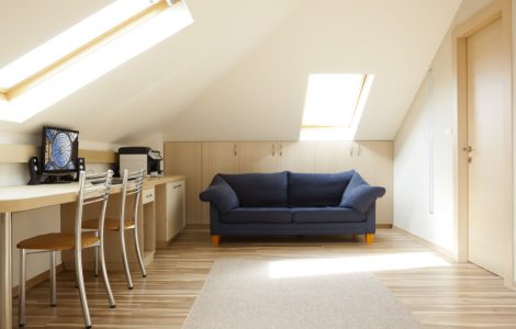 Une chambre aménagée dans le grenier avec un canapé bleu et un coin bureau