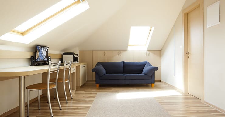 Une chambre aménagée dans le grenier avec un canapé bleu et un coin bureau