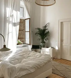 Vue sur une chambre aux tons blancs et une suspension en rotin