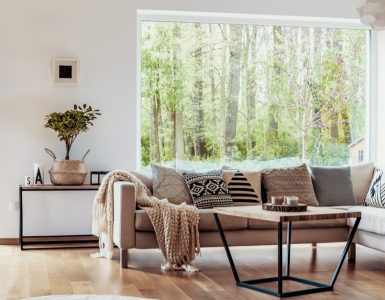 Salon avec canapé beige, parquet en bois et grandes baies vitrées