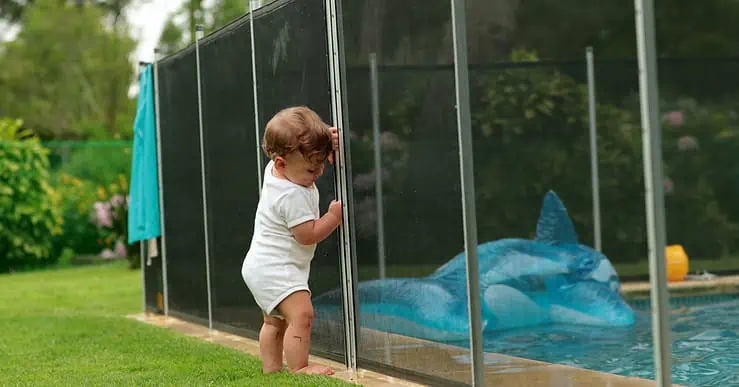 Un bébé s'appuyant sur une clôture de piscine