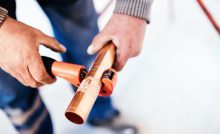 Zoom sur les mains d'un homme coupant un tuyau en cuivre avec un coupe-tuyau