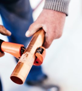 Zoom sur les mains d'un homme coupant un tuyau en cuivre avec un coupe-tuyau