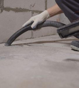 Un homme en gants blancs nettoie le sol avec un aspirateur après le chantier