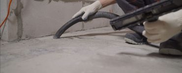 Un homme en gants blancs nettoie le sol avec un aspirateur après le chantier