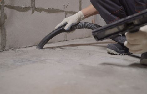 Un homme en gants blancs nettoie le sol avec un aspirateur après le chantier