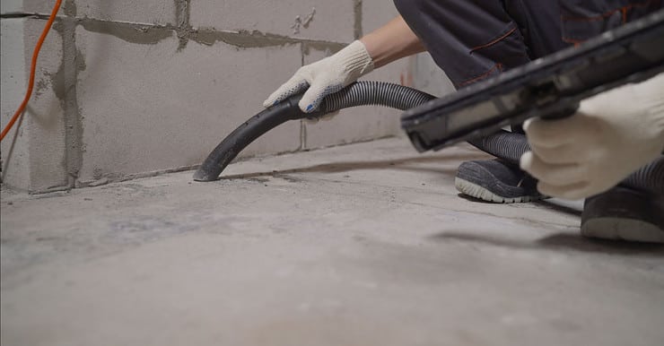 Un homme en gants blancs nettoie le sol avec un aspirateur après le chantier