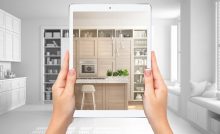 Mains tenant une tablette montrant une cuisine moderne blanche et en bois