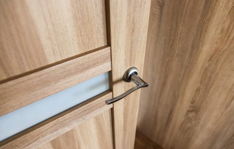 Zoom sur les détails d’une porte en bois clair et sa poignée chromée