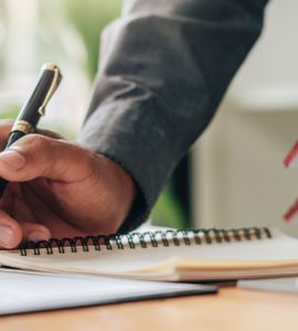 Un homme tenant un stylo en train de lire des documents, avec une maquette de maison sur la table