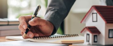 Un homme tenant un stylo en train de lire des documents, avec une maquette de maison sur la table