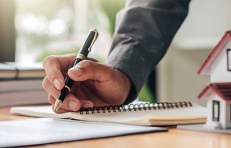 Un homme tenant un stylo en train de lire des documents, avec une maquette de maison sur la table