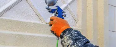 Zoom sur la main d’un homme en train de peindre un mur avec un pistolet à air comprimé