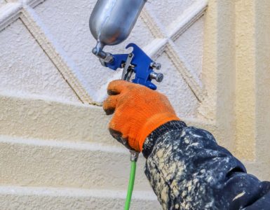 Zoom sur la main d’un homme en train de peindre un mur avec un pistolet à air comprimé
