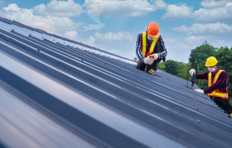 Deux ouvriers avec des gilets et des casques de chantier en train de fixer le revêtement de toit