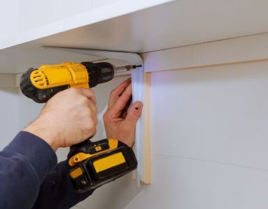 Zoom sur les mains d'un homme installant des étagères en bois sur un mur avec sa visseuse