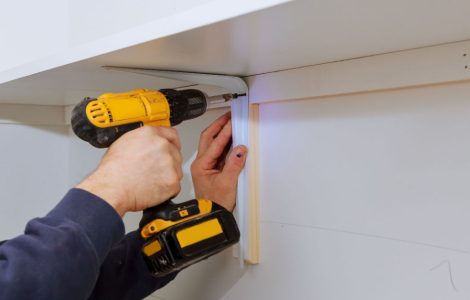 Zoom sur les mains d'un homme installant des étagères en bois sur un mur avec sa visseuse