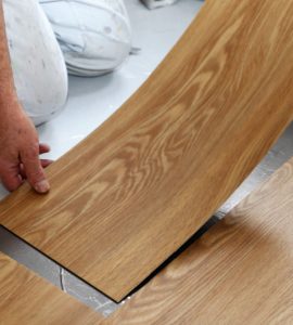 Un homme à genoux installant le sol en PVC effet bois