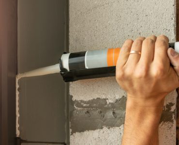 Un homme applique un joint en silicone avec un pistolet sur les bords d'une fenêtre