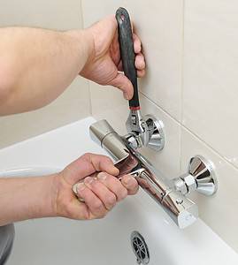 Un homme utilise une clé pour resserrer le mitigeur de la salle de bain