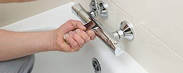 Un homme utilise une clé pour resserrer le mitigeur de la salle de bain