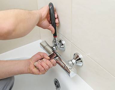 Un homme utilise une clé pour resserrer le mitigeur de la salle de bain