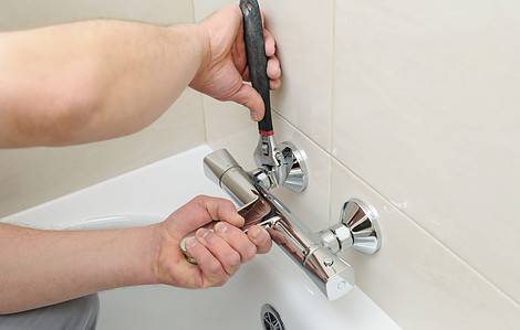 Un homme utilise une clé pour resserrer le mitigeur de la salle de bain