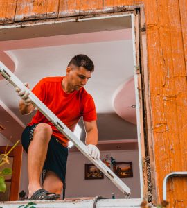 Un homme debout sur une fenêtre pour remplacer les cadres de la fenêtre