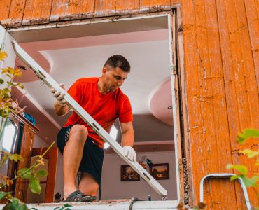 Un homme debout sur une fenêtre pour remplacer les cadres de la fenêtre