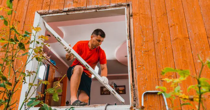 Un homme debout sur une fenêtre pour remplacer les cadres de la fenêtre