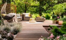 Une terrasse en bois avec mobilier de jardin entourée de fleurs et d’arbres