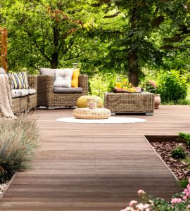 Une terrasse en bois avec mobilier de jardin entourée de fleurs et d’arbres