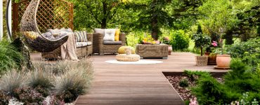 Une terrasse en bois avec mobilier de jardin entourée de fleurs et d’arbres