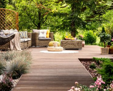 Une terrasse en bois avec mobilier de jardin entourée de fleurs et d’arbres