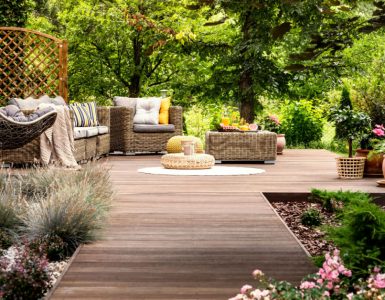 Une terrasse en bois avec mobilier de jardin entourée de fleurs et d’arbres