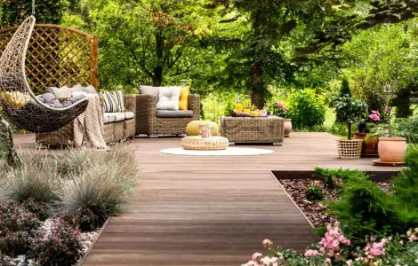 Une terrasse en bois avec mobilier de jardin entourée de fleurs et d’arbres