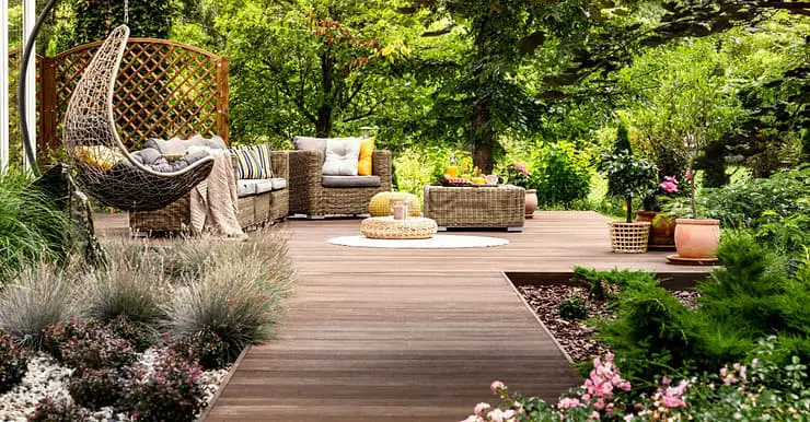 Une terrasse en bois avec mobilier de jardin entourée de fleurs et d’arbres