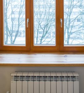 Un radiateur de chauffage placé sous une fenêtre en bois